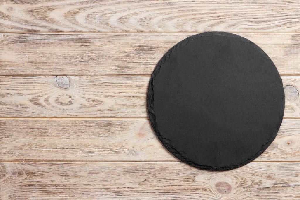 Black slate round stone on wooden background, top view, copy space.